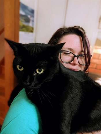 A black cat adorably obscures most of Caitlin Archer-Helke's patiently smiling face